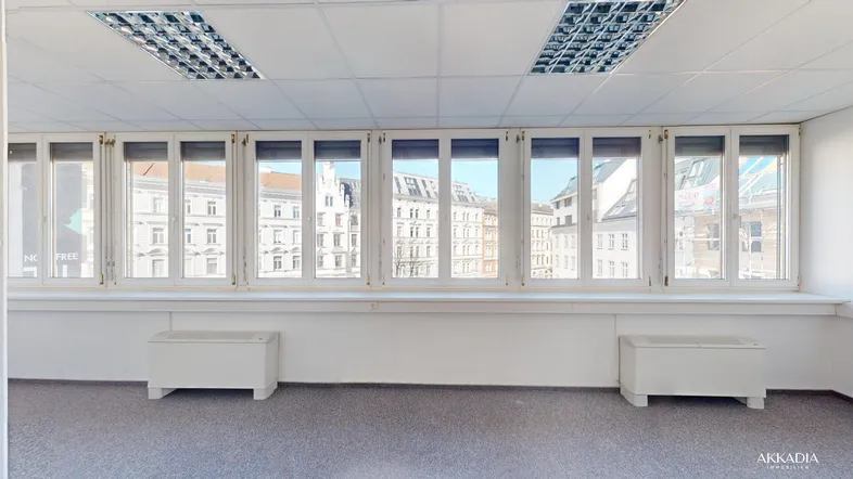Heller Büroraum mit vielen Fenstern, Teppichboden und Blick auf die Stadtgebäude.