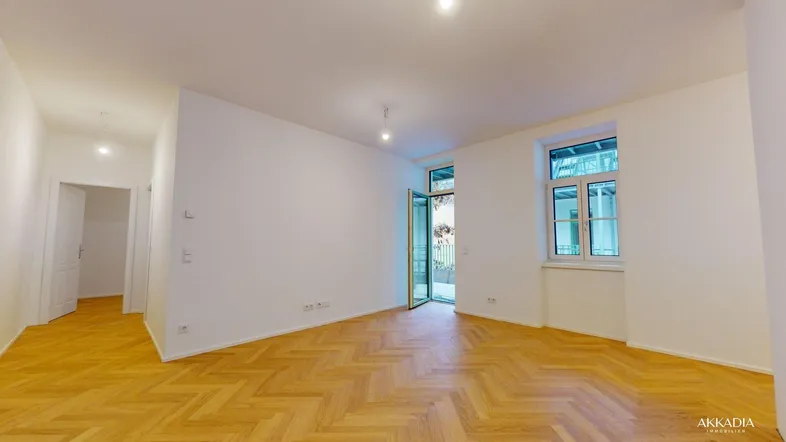 Helles, leeres Zimmer mit Fischgrätparkett und Zugang zu einem Außenbereich, ideal als Wohnzimmer.