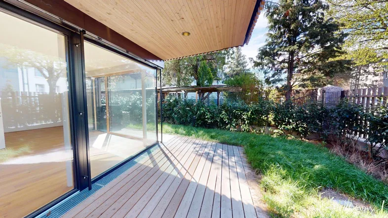 Moderne Holzterrasse mit direktem Zugang zu einem lichtdurchfluteten Innenraum durch große Glasfronten.