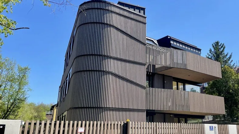 Modernes Gebäude mit geschwungener Holzfassade und Balkonen unter blauem Himmel.