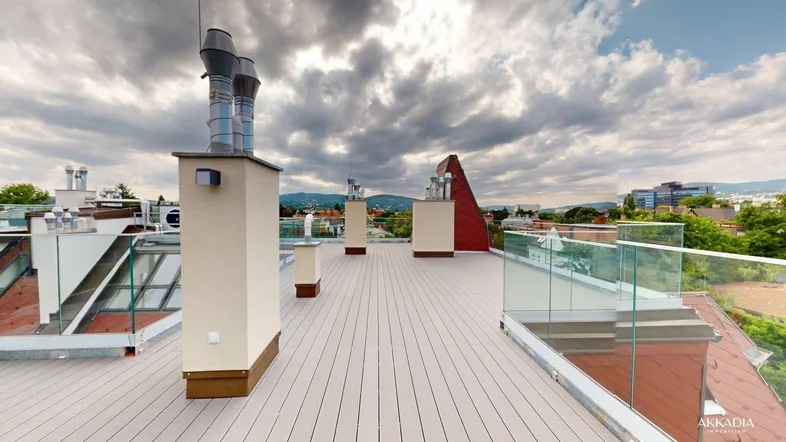 Geräumige Dachterrasse mit Holzbelag, Glasgeländer und weitem Blick über die Stadt und grüne Hügel.