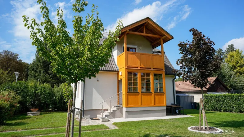 Charmantes Einfamilienhaus mit gepflegtem Garten und traditionellem Holzbalkon unter blauem Himmel.