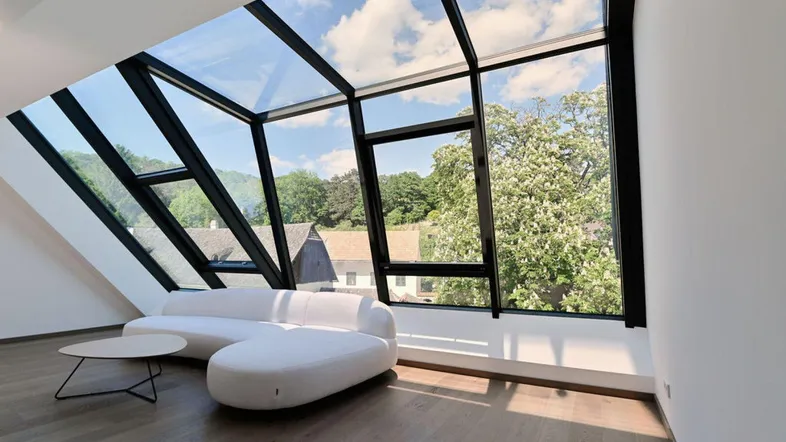 Helles Wohnzimmer mit moderner Couch und beeindruckender Glasfassade mit Blick ins Grüne.