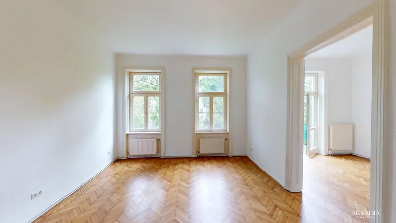 Helles Wohnzimmer mit Fischgrätparkettboden, hohen Decken und zwei großen Fenstern.