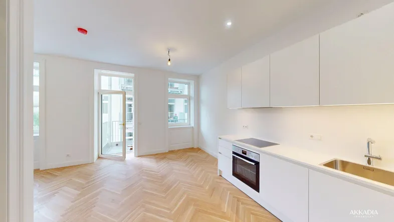 Heller offener Wohnbereich mit integrierter Küche, Fischgrätparkett und Zugang zu einem französischen Balkon.