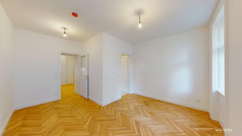 Helles, leeres Zimmer mit Fischgrätparkett und weißen Wänden, bereit zur individuellen Gestaltung.