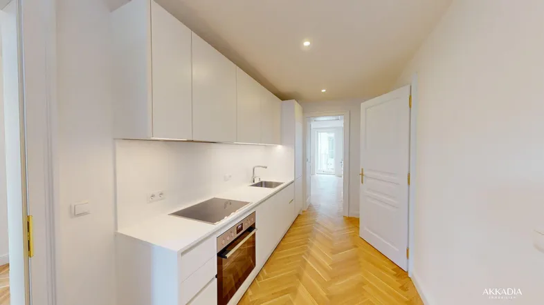 Moderne, helle Küche mit weißen Schränken, integrierten Geräten und Fischgrätparkettboden.