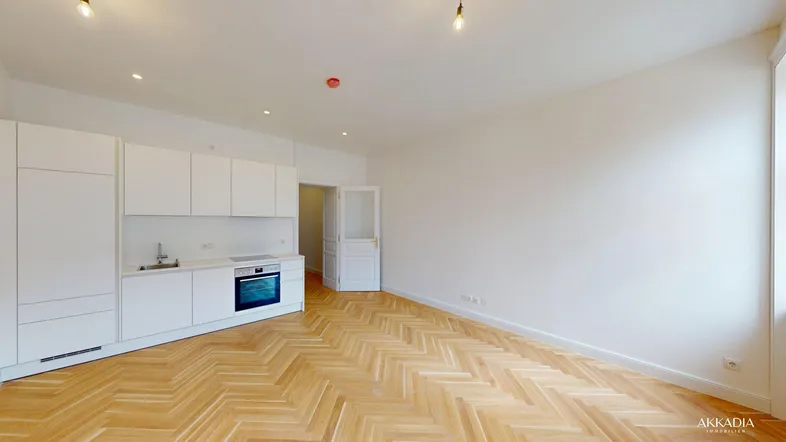 Helles Wohnzimmer mit integrierter Küchenzeile und elegantem Fischgrätparkettboden.