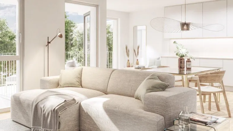 Helles, offenes Wohn-Esszimmer mit moderner Küche, beigem Sofa und Zugang zu einem Balkon.