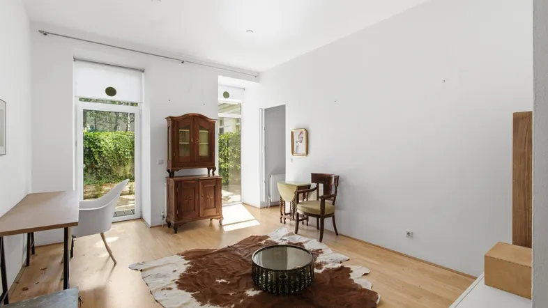 Helles Wohnzimmer mit Holzboden, weiß gestrichenen Wänden und direktem Zugang zu einem Außenbereich.