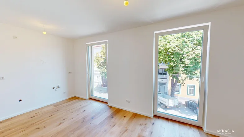 Helles, unmöbliertes Zimmer mit Parkettboden und großen Fenstern, die viel Tageslicht hereinlassen.