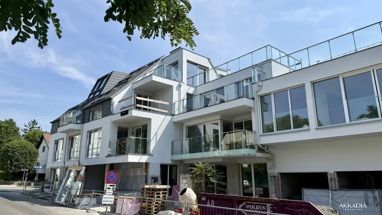 Modernes Mehrfamilienhaus im Bau mit großen Fensterfronten, Balkonen und Dachterrassen.