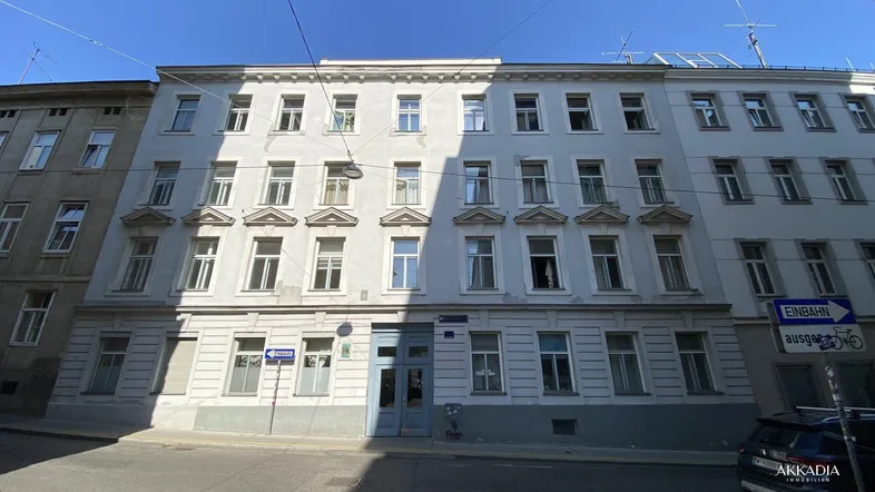 Fassade eines klassischen Altbaus mit vielen Fenstern und schattiger Straßenseite.