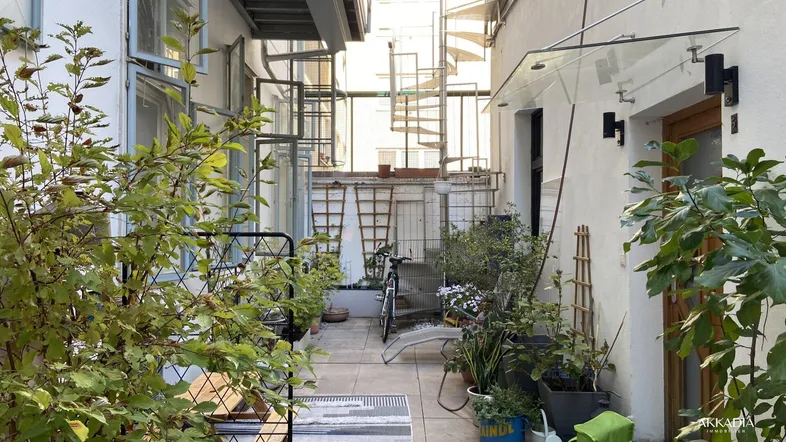Hinterhof-Terrasse mit Pflanzen, Sitzgelegenheiten und Blick auf eine Wendeltreppe in einem Innenhof.