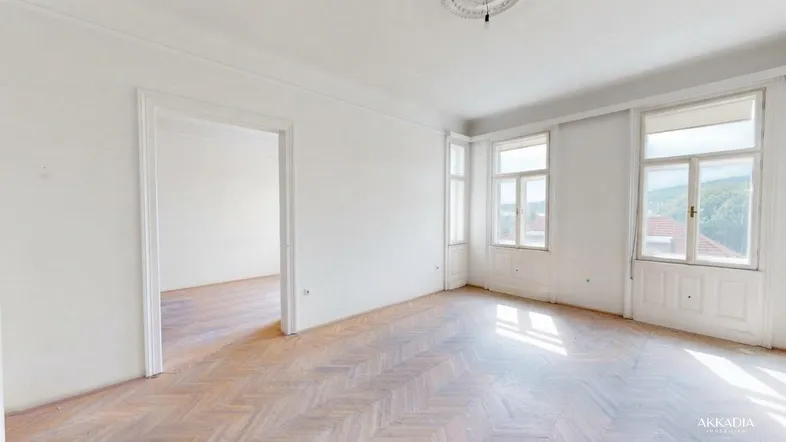 Helles, leeres Zimmer mit Fischgrätparkett und großen Fenstern, die viel Tageslicht hereinlassen.
