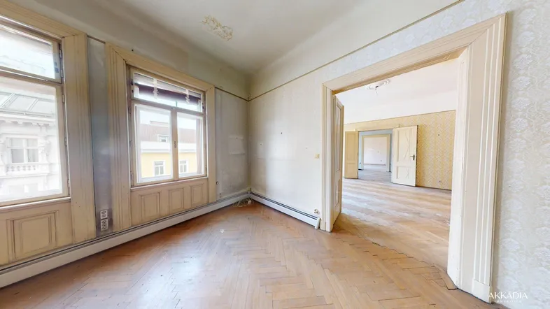 Geräumiges Zimmer mit Fischgrätparkett und hohen Fenstern, das Renovierungsbedarf aufweist.