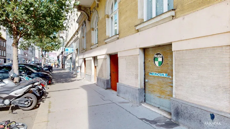 Straßenansicht eines Gebäudes mit Geschäften im Erdgeschoss und parkenden Motorrädern am Gehweg.