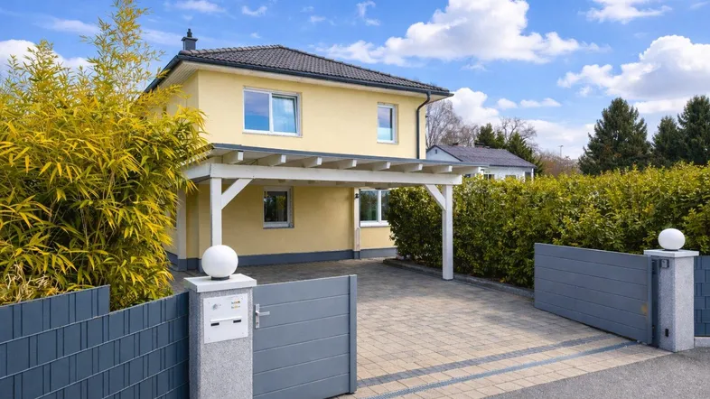 Einfamilienhaus mit Carport und gepflegtem Vorgarten unter blauem Himmel.