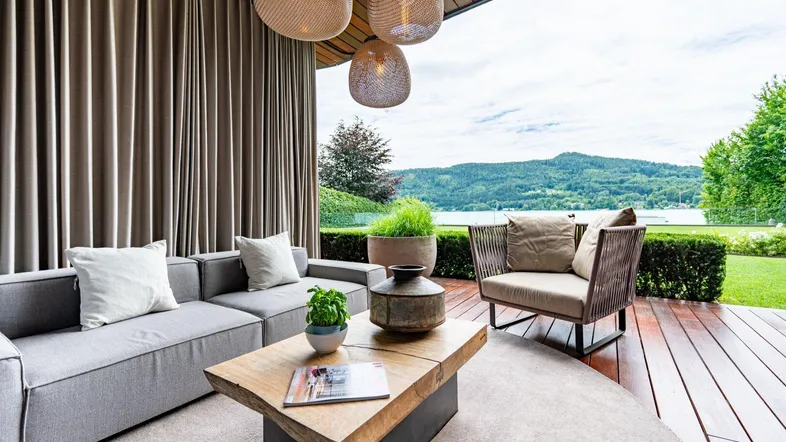 Überdachte Terrasse mit bequemen Loungemöbeln und weitem Blick auf den See und die Berge.