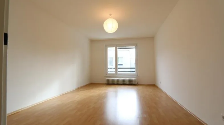 Helles, leeres Zimmer mit Parkettboden und einem Fenster, bereit zur individuellen Gestaltung.