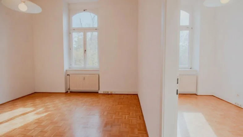 Helles Zimmer mit Parkettboden, hohen Decken und großen Bogenfenstern.
