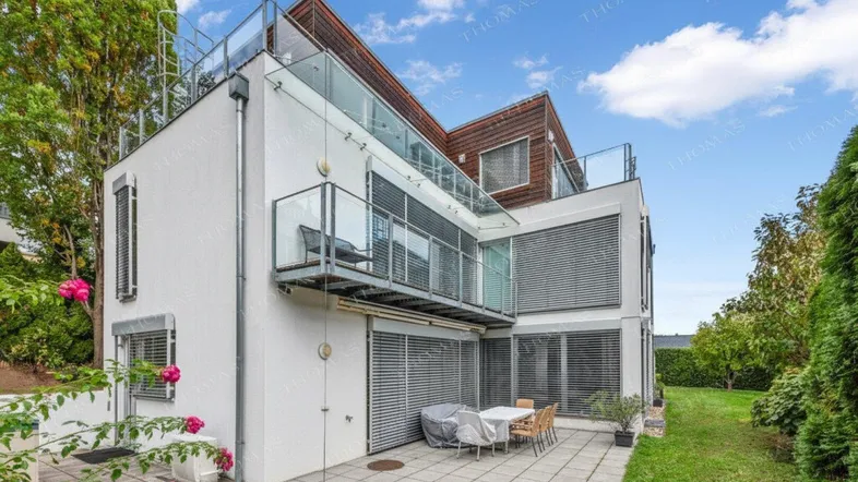 Ansicht des modernen Hauses von der Seite mit Terrasse, Garten und großen Fenstern.
