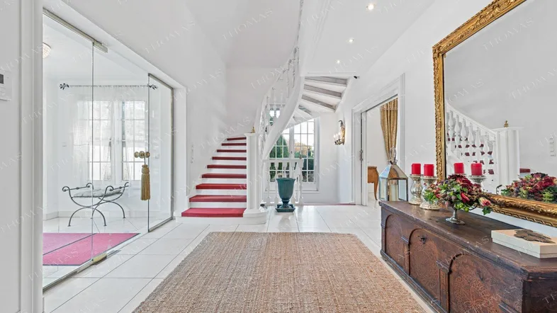 Heller Eingangsbereich mit eleganter Wendeltreppe, Fliesenboden und großem Spiegel.