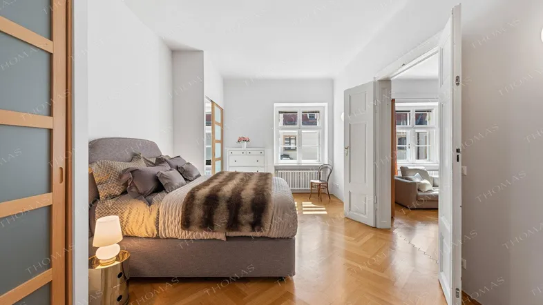 Helles Schlafzimmer mit Parkettboden, großem Bett und Zugang zu einem angrenzenden Raum.