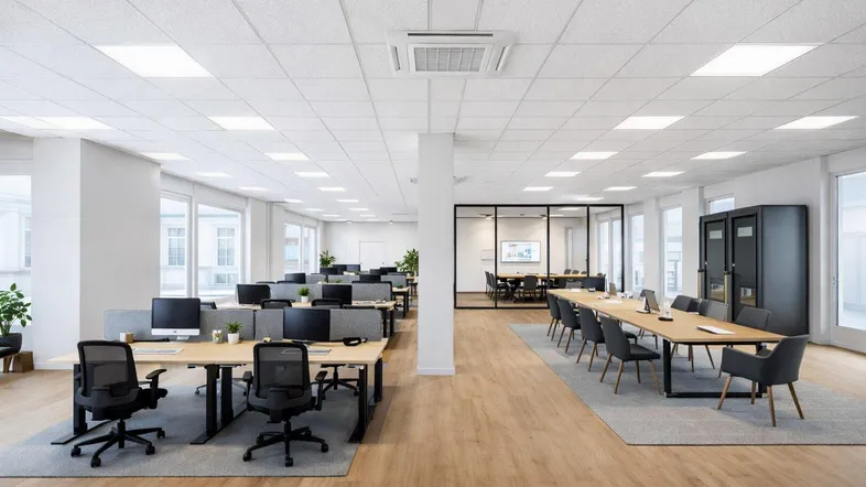 Modernes Großraumbüro mit hellen Arbeitsplätzen, einem Konferenzraum mit Glaswänden und großen Fenstern für viel Tageslicht.