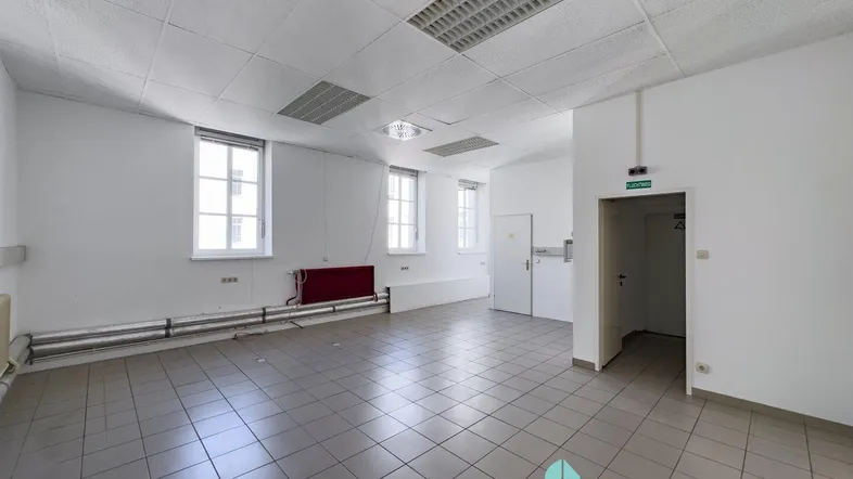Geräumiger, leerer Büroraum mit Fliesenboden, großen Fenstern und abgehängter Decke.