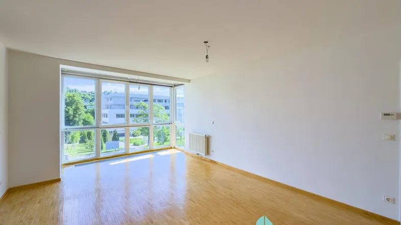 Helles, leeres Wohnzimmer mit großen Fenstern und Blick ins Grüne, ausgestattet mit Parkettboden.