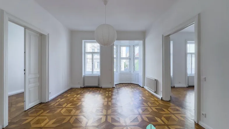 Geräumiges Wohnzimmer mit elegantem Fischgrätparkett, hohen Decken und großen Fenstern, die viel Licht hereinlassen.