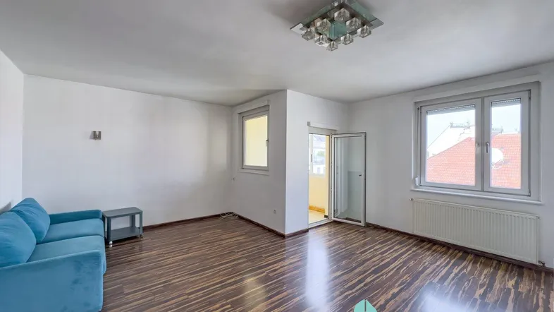 Helles Wohnzimmer mit dunklem Laminatboden, einem blauen Sofa und Zugang zu einem Balkon.