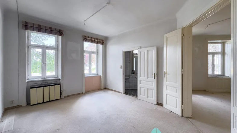 Geräumiges Zimmer mit Teppichboden, hohen Decken und zwei großen Fenstern, die viel Licht hereinlassen.