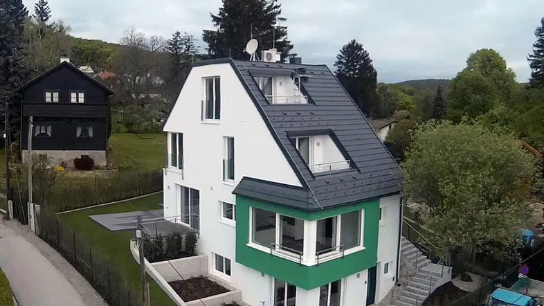 Modernes Einfamilienhaus mit weißer und grüner Fassade, umgeben von viel Grün und anderen Häusern.