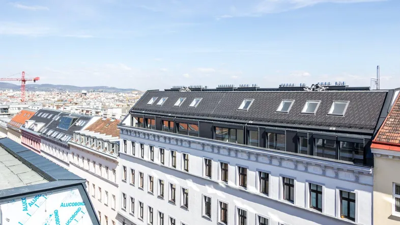 Blick über die Dächer der Stadt mit modernen Dachfenstern und einem Kran in der Ferne.