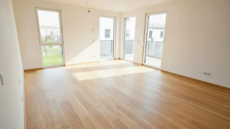 Helles, leeres Zimmer mit neuem Parkettboden und Zugang zu einem Balkon oder Garten.