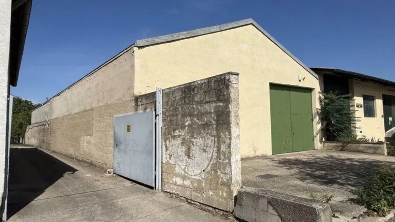 Ansicht eines Lagergebäudes mit beiger Fassade, großem grünen Tor und einem Zufahrtsweg.