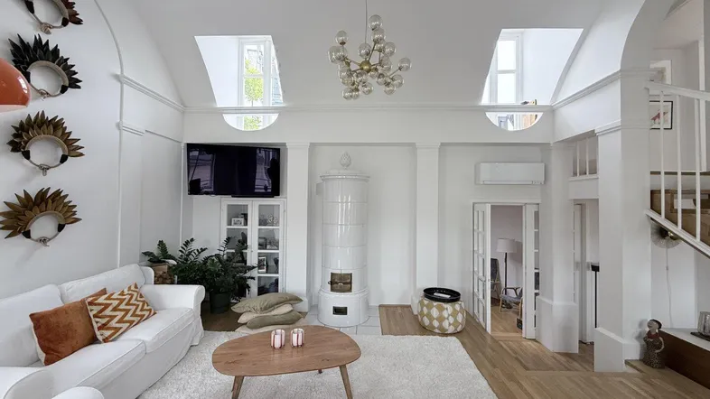 Helles Wohnzimmer mit hohen Decken, weißem Kachelofen und Holzboden, modern eingerichtet.