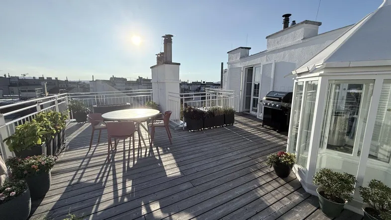 Große Dachterrasse mit Holzbelag, Gartenmöbeln und Grill, ideal für sonnige Tage mit Stadtblick.