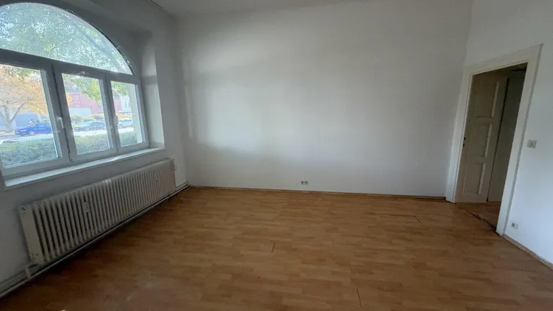 Helles Zimmer mit Holzboden, weißen Wänden und einem großen Bogenfenster, das viel Licht hereinlässt.