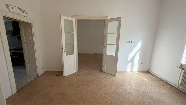 Helles Zimmer mit Fischgrätparkett und Flügeltüren, bereit zur Renovierung.