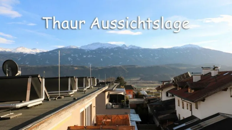 Panoramablick über Dächer und schneebedeckte Berge unter blauem Himmel mit Solarpanelen.