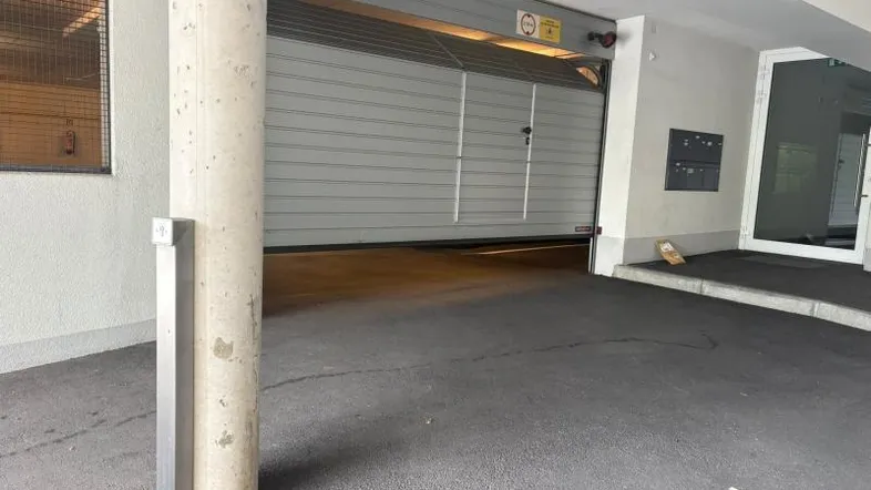 Einfahrt zu einer Tiefgarage mit geöffnetem Rolltor und Betonpfeiler in modernem Design.