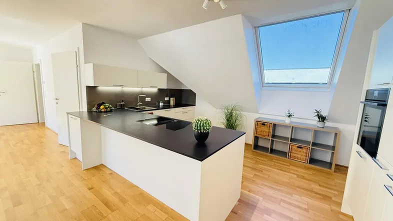 Moderne offene Küche mit Kücheninsel, Holzboden und Dachfenster in einem hellen Dachgeschoss.