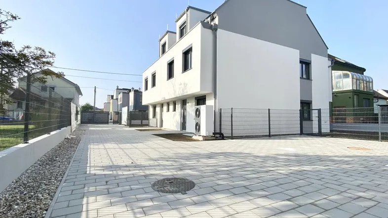 Moderne Reihenhäuser mit gepflastertem Vorplatz und klaren Linien unter blauem Himmel.