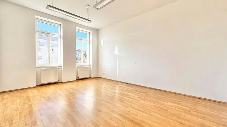 Helles, leeres Zimmer mit glänzendem Parkettboden, weißen Wänden und modernen Deckenleuchten.
