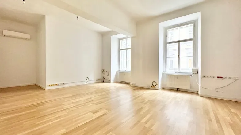 Geräumiger, heller Büroraum mit Holzboden, hohen Decken und großen Fenstern, bereit zur individuellen Gestaltung.