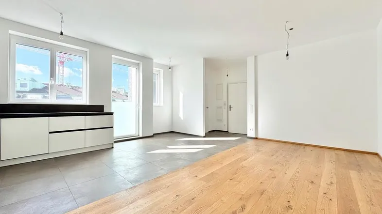Helles, offenes Wohnzimmer mit Holzboden und Fliesenbereich, vorbereitet für eine moderne Küche.