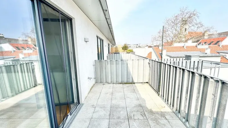 Geräumiger Balkon mit Fliesenboden und Metallgeländer, bietet einen weiten Blick über die Dächer der Stadt.